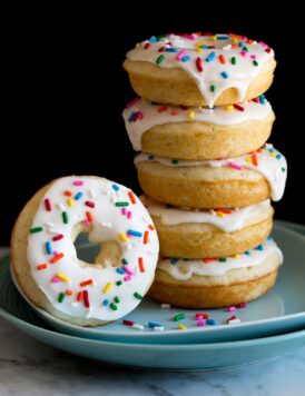 Image of stack of baked donuts on a plate. They are covered in icing and sprinkles.