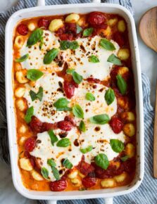 Baked Gnocchi in a white baking dish with marinara sauce, mozzarella and basil.