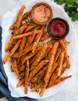 Baked sweet potato fries on a white oval platter with dipping sauces on the side.