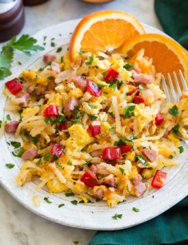 Photo: Serving of breakfast hash on a white ceramic plate with oranges to the side. Hash is made with shredded hash browns, ham, eggs, bell pepper, parsley and onion.