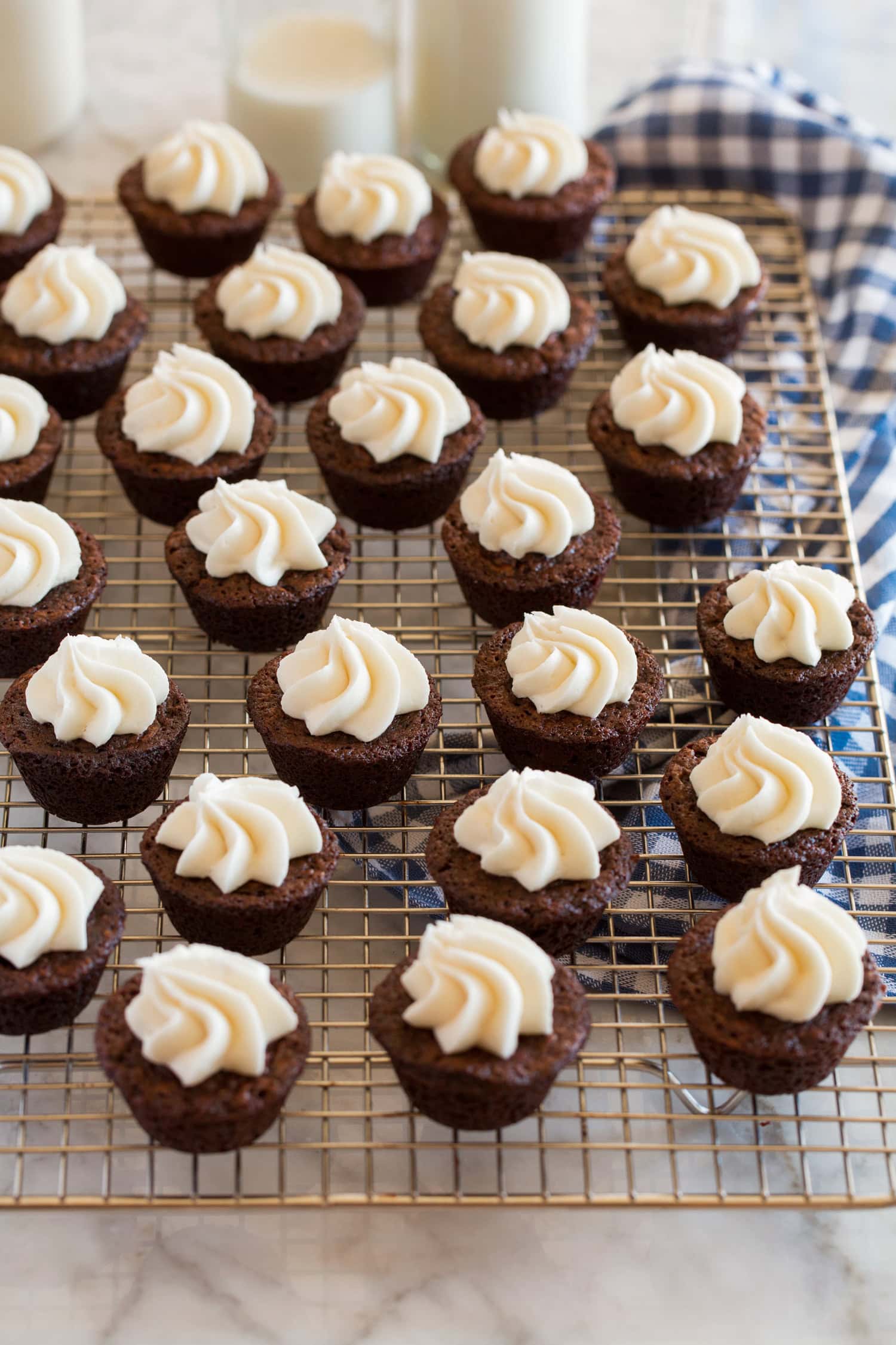 Cream cheese frosting topped brownie bites on a wire cooling rack.