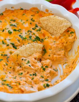 Buffalo chicken dip in a ceramic white pie dish. Shown with tortilla chips dipped in.