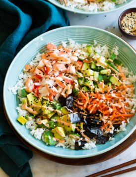 California roll sushi bowl shown in a blue bowl from a side angle. Bowl is resting on a wooden plate over a marble surface.