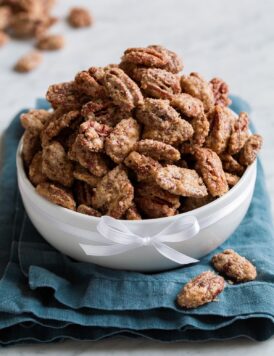 Candied pecans mounded high in a white bowl set over a blue cloth.