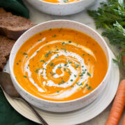 Single serving of carrot soup in a soup bowl with a second serving shown in the background.