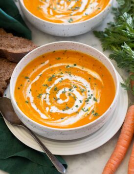 Single serving of carrot soup in a soup bowl with a second serving shown in the background.