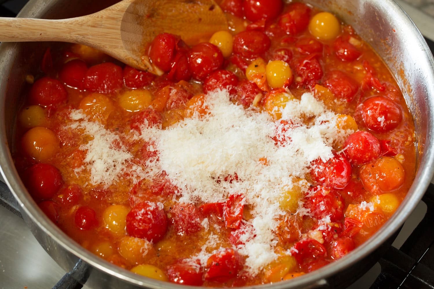 Burst cherry tomato sauce with parmesan being added.