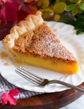 Slice of chess pie on a white dessert plate with fall leaves surrounding plate.