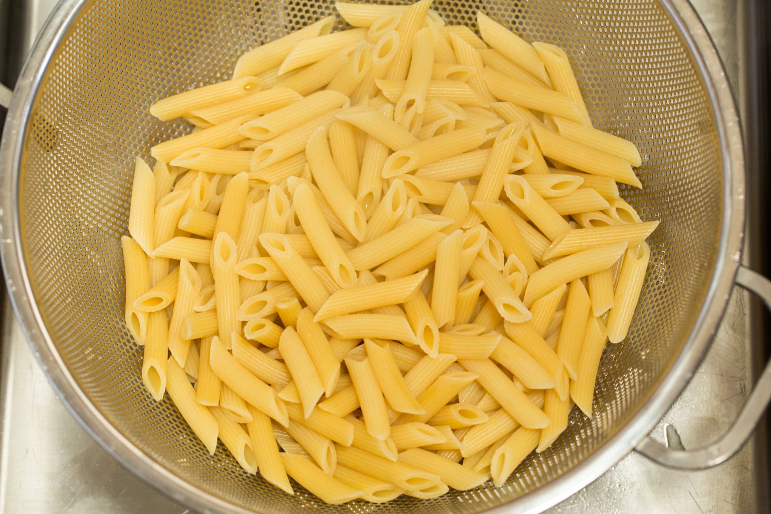 Cooked penne pasta draining in a colander.