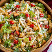 Side angle shown of chicken caesar pasta salad with romaine lettuce, chicken, croutons, parmesan and tomatoes.