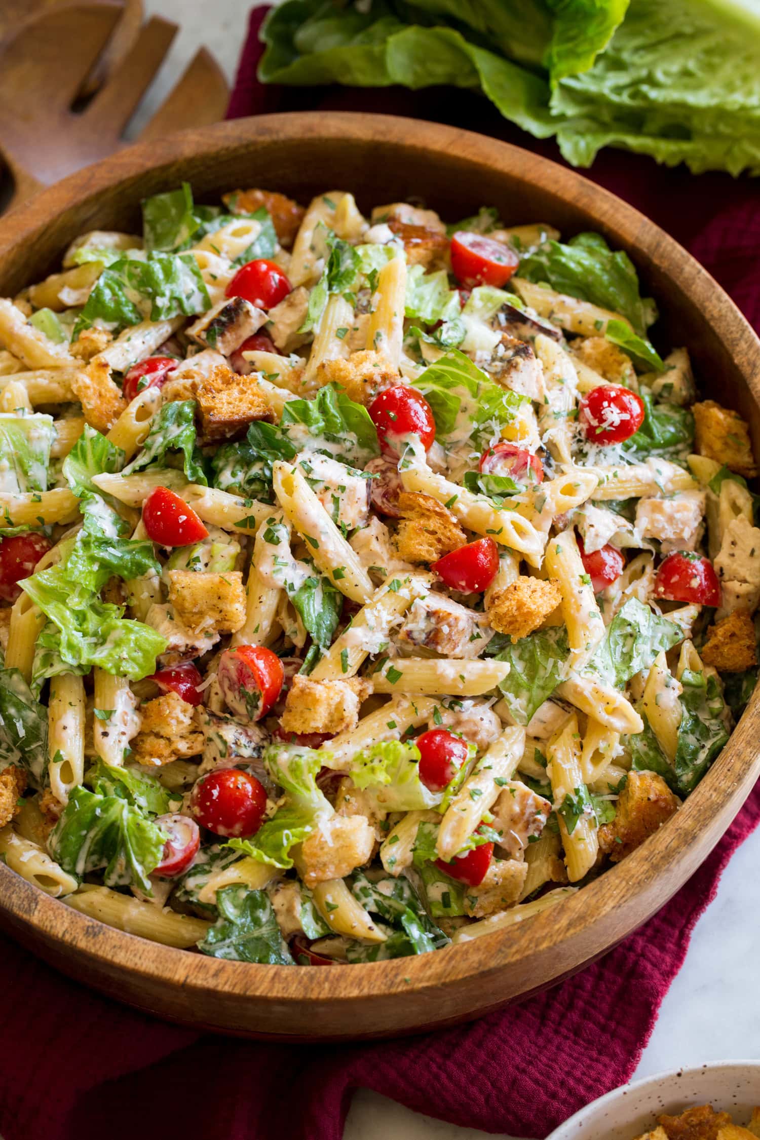 Side angle shown of chicken caesar pasta salad with romaine lettuce, chicken, croutons, parmesan and tomatoes.