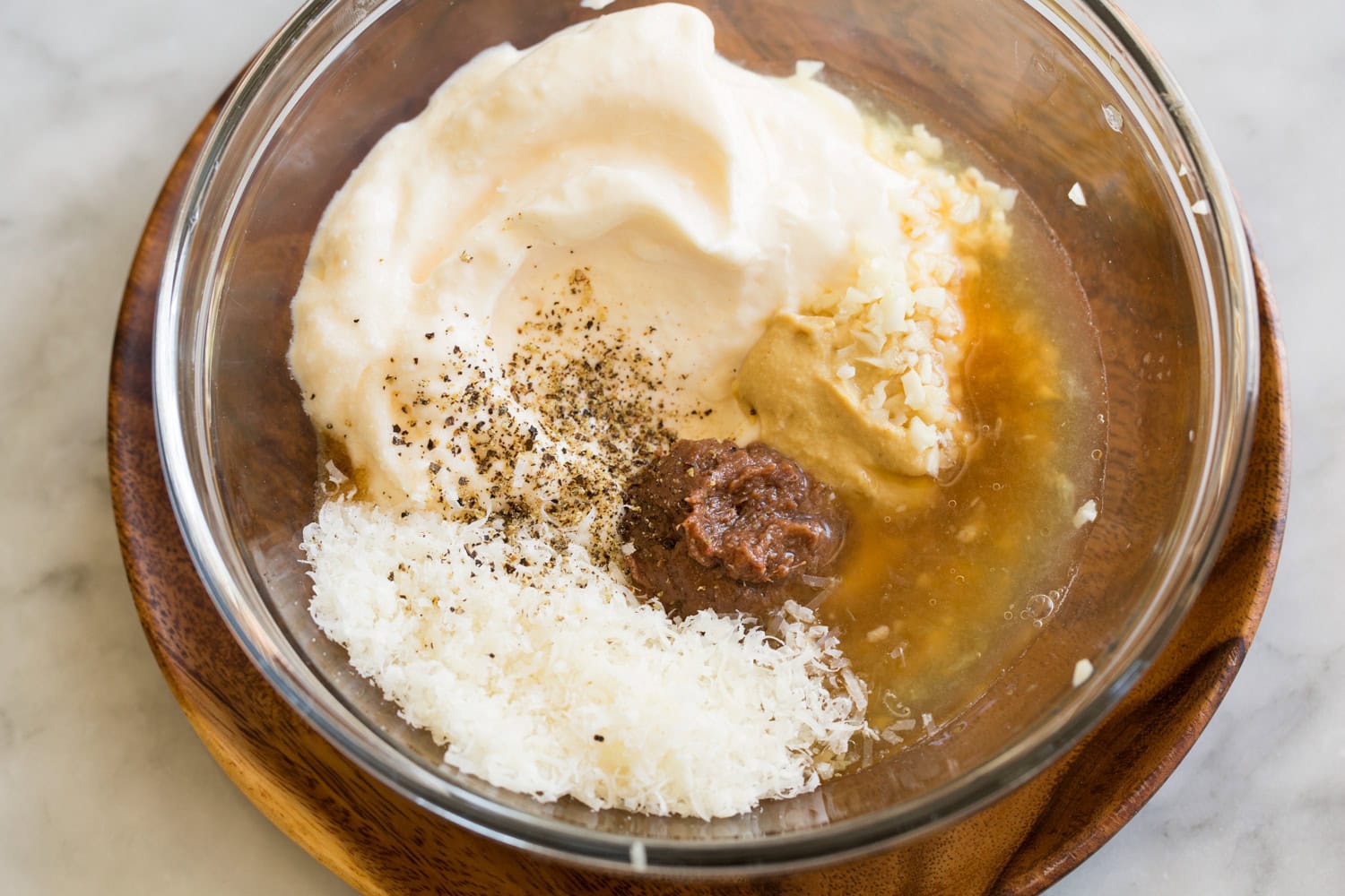 Ingredients for caesar dressing in a glass mixing bowl shown before mixing.