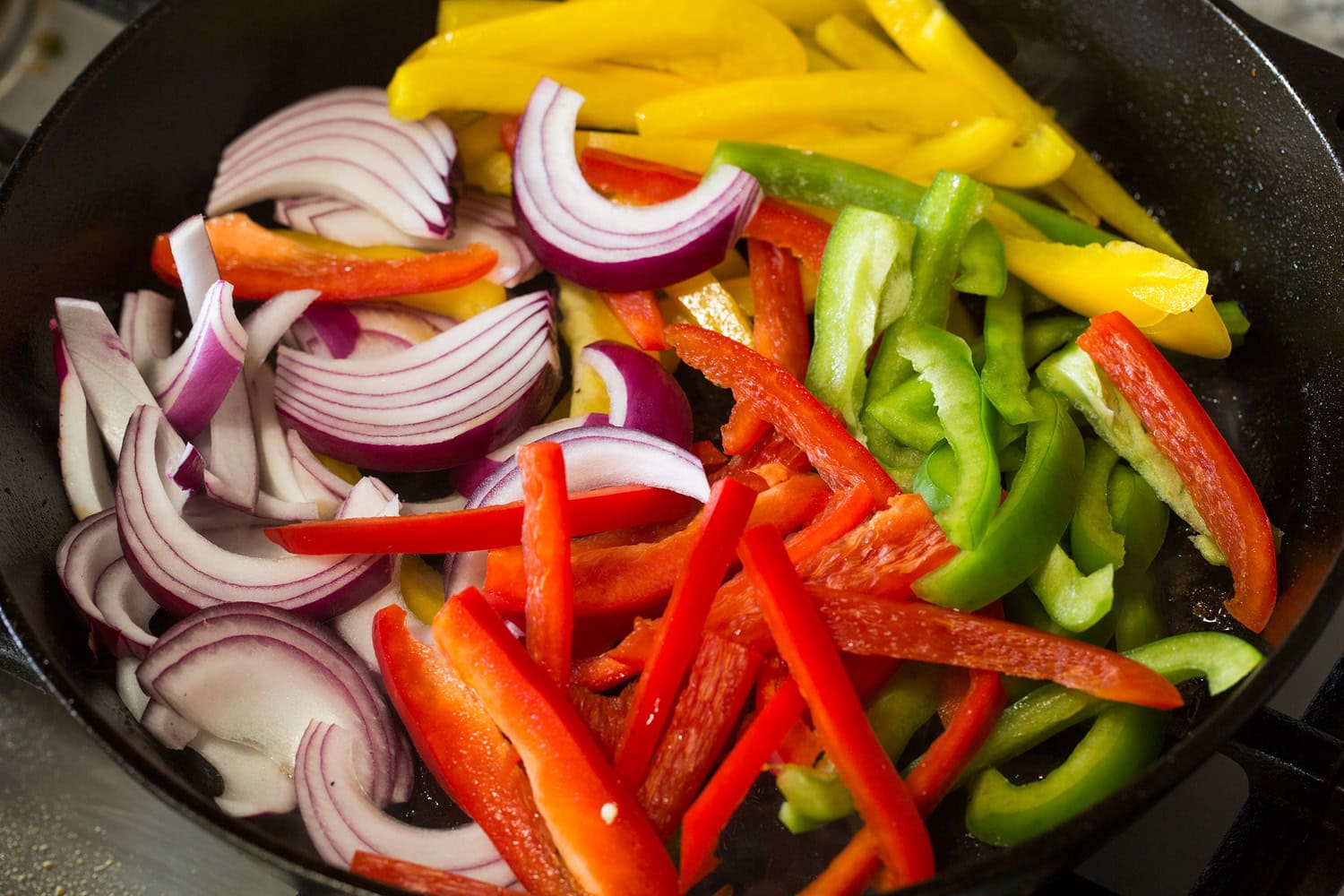 Sliced bell peppers and onions shown in skillet before cooking.