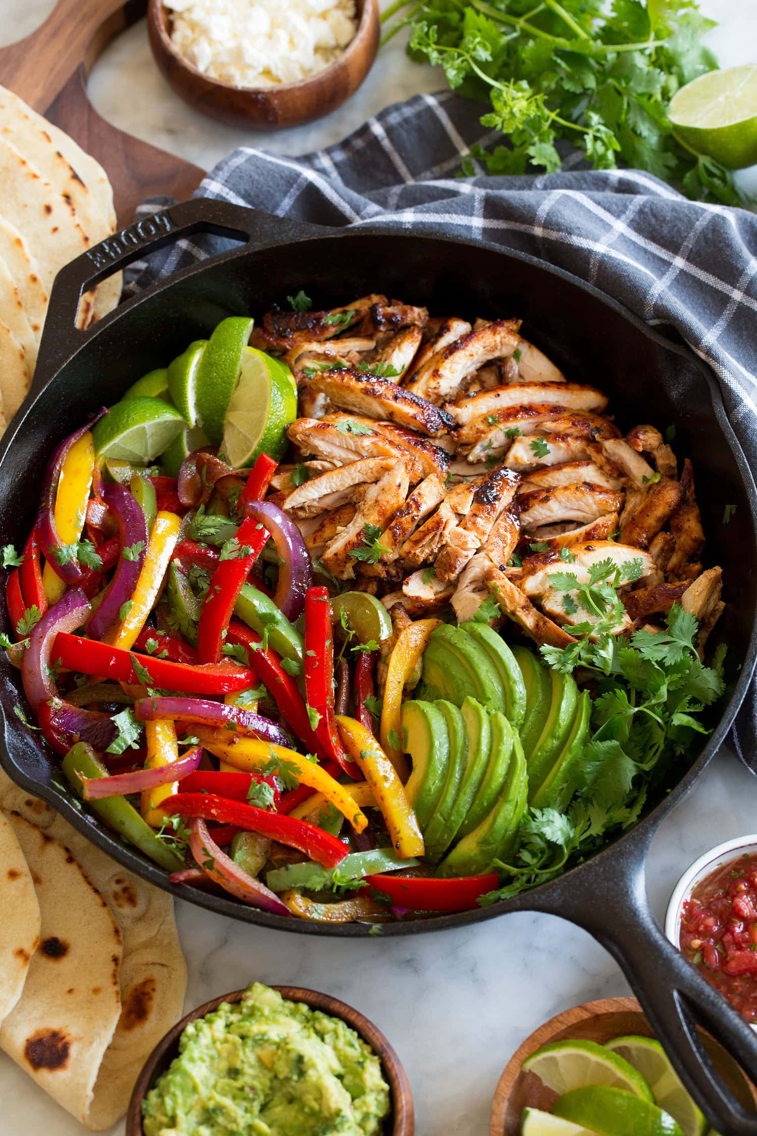 Chicken and bell peppers in a cast iron skillet with cilantro, avocado and limes.