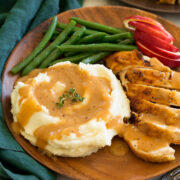 Chicken gravy shown on mashed potatoes with a side of roasted chicken, apples and green beans as a serving suggestion.