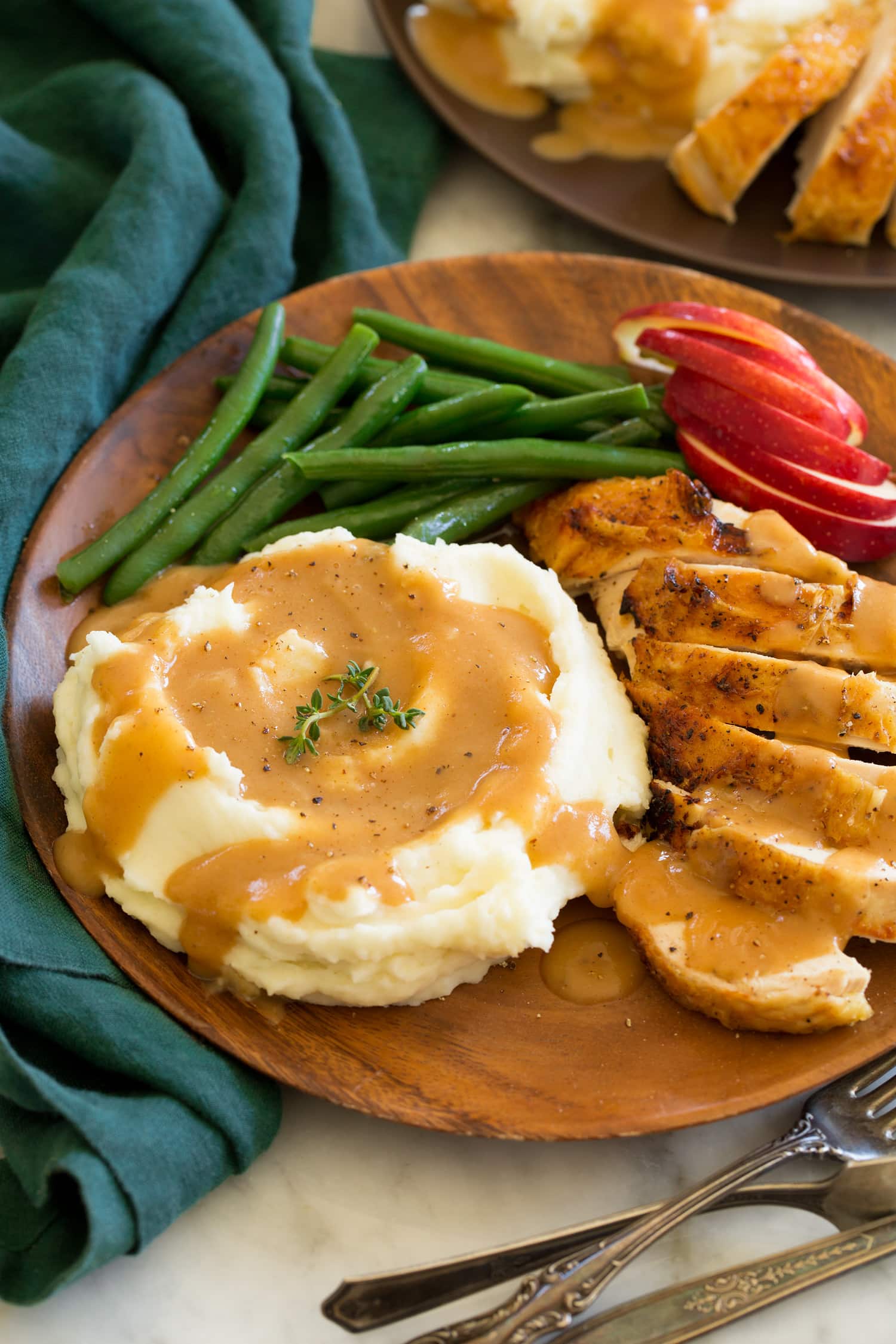 Chicken gravy shown on mashed potatoes with a side of roasted chicken, apples and green beans as a serving suggestion.