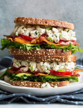 Stack of two chicken salad sandwiches on a white plate set over a dark grey cloth.