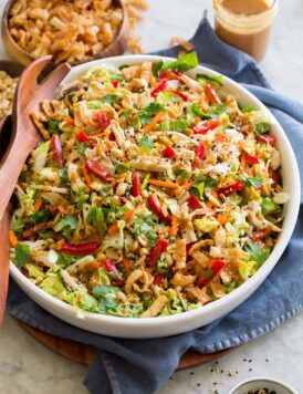 Large serving bowl full of Chinese chicken salad with cabbage, peanuts, sesame seeds, wonton strips, bell peppers.