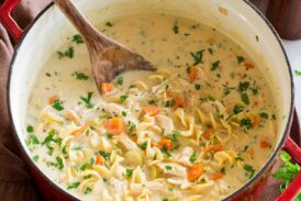 Pot full of homemade creamy chicken noodle soup served with a side of bread.