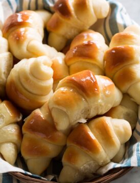 Homemade dinner rolls shown in a basket with a blue striped cloth.