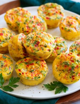 Egg muffins shown on a white serving platter over a wooden platter and a blue cloth.