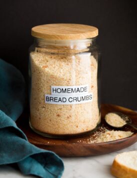 Image: homemade plain bread crumbs in a glass jar set on a wooden plate with a black background.