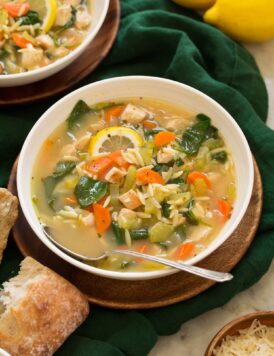 Lemon Chicken Orzo Soup in a white serving bowl on a wooden plate.