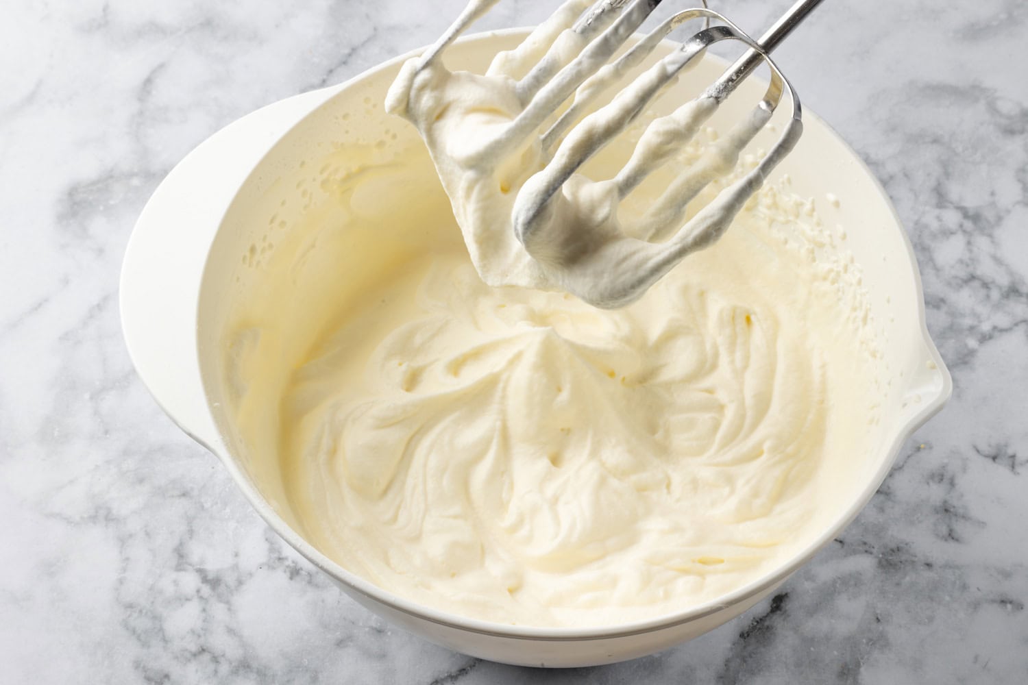 Whipped cream in bowl shown with electric beaters.