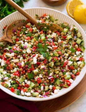 Lentil salad shown in a white ceramic serving bowl. Made with green lentils, bell pepper, red onion, feta, cucumber and dressing.