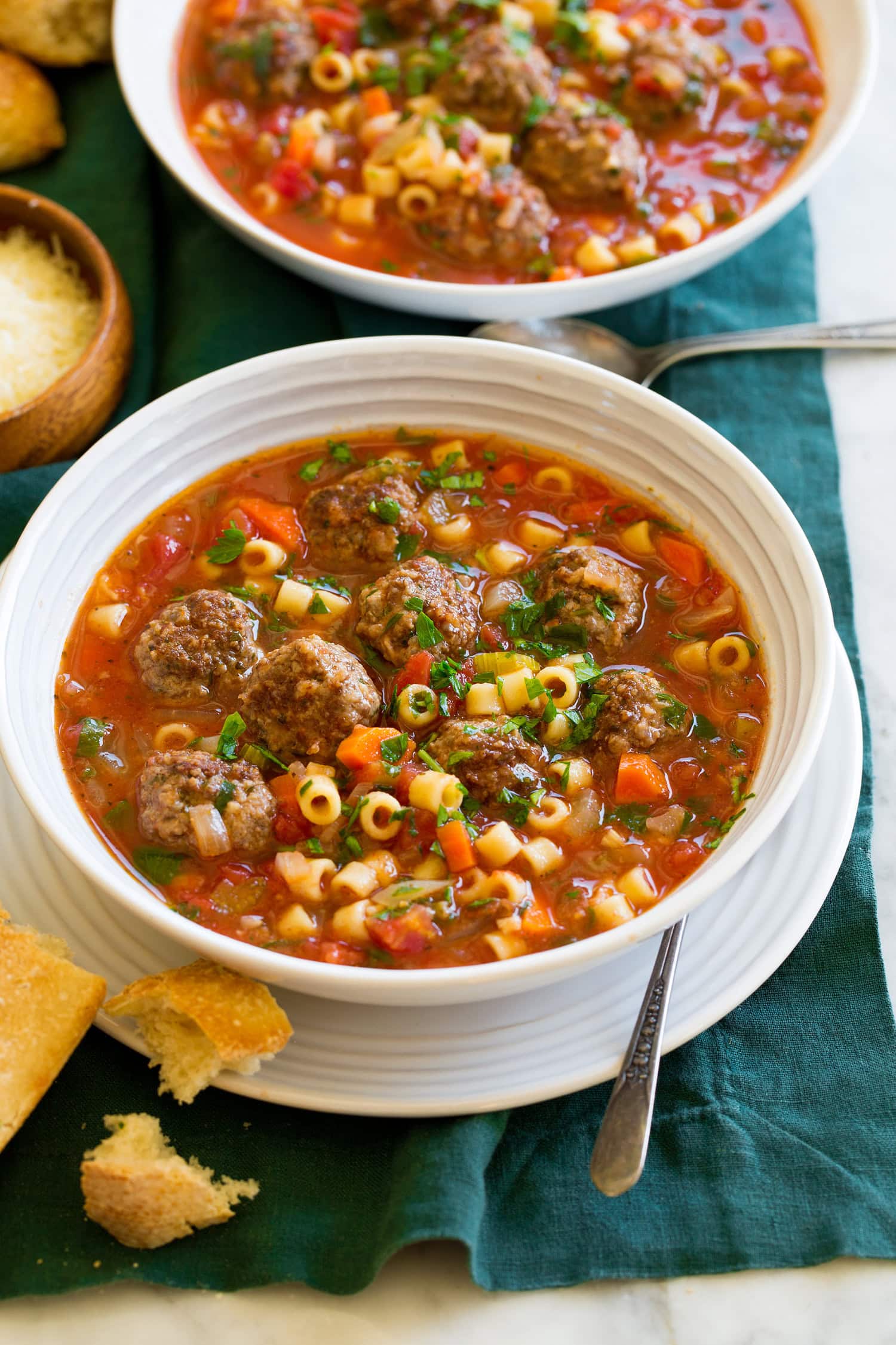 Serving of meatball soup in a white bowl over a white plate with bread to the side.