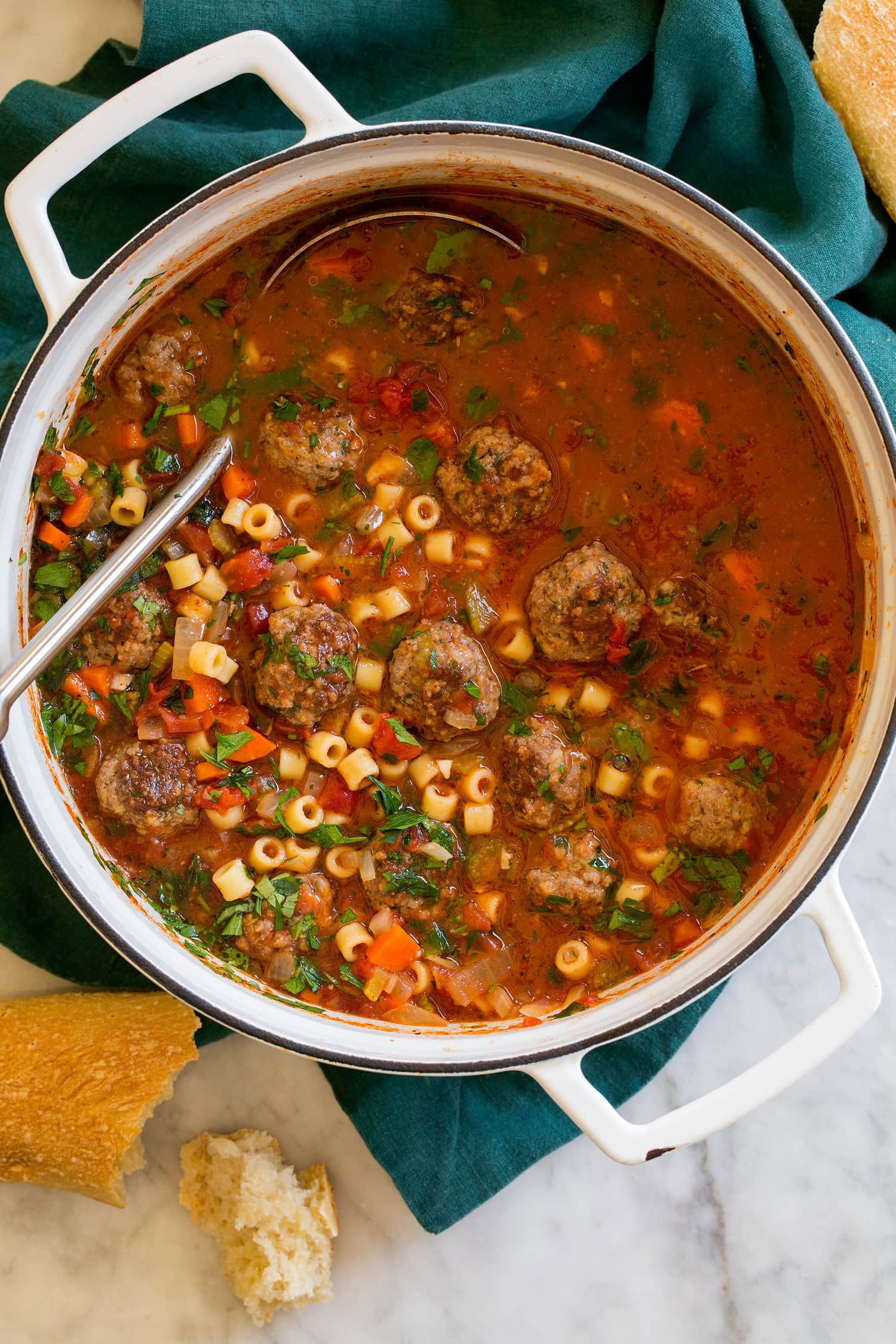 Overhead photo of meatball soup in a white pot over a blue cloth.