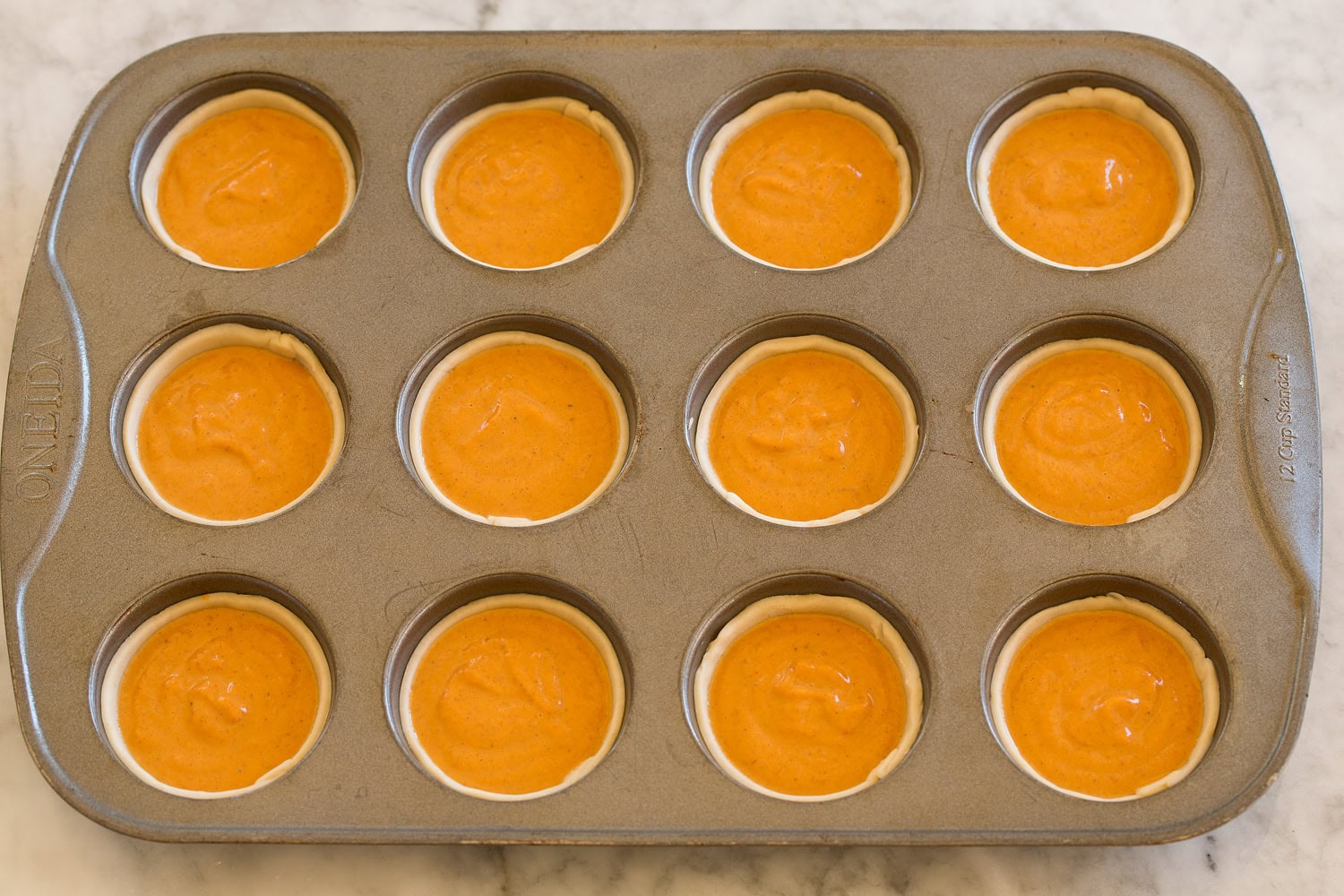 Pumpkin pie filling poured into mini pie crusts in muffin pan.