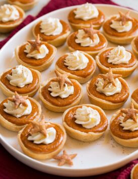 Platter filled with many mini pumpkin pies topped with whipped cream and cinnamon.