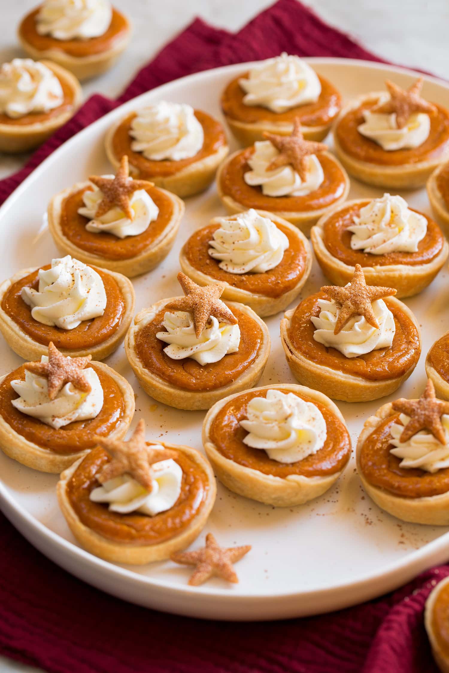 Platter filled with many mini pumpkin pies topped with whipped cream and cinnamon.