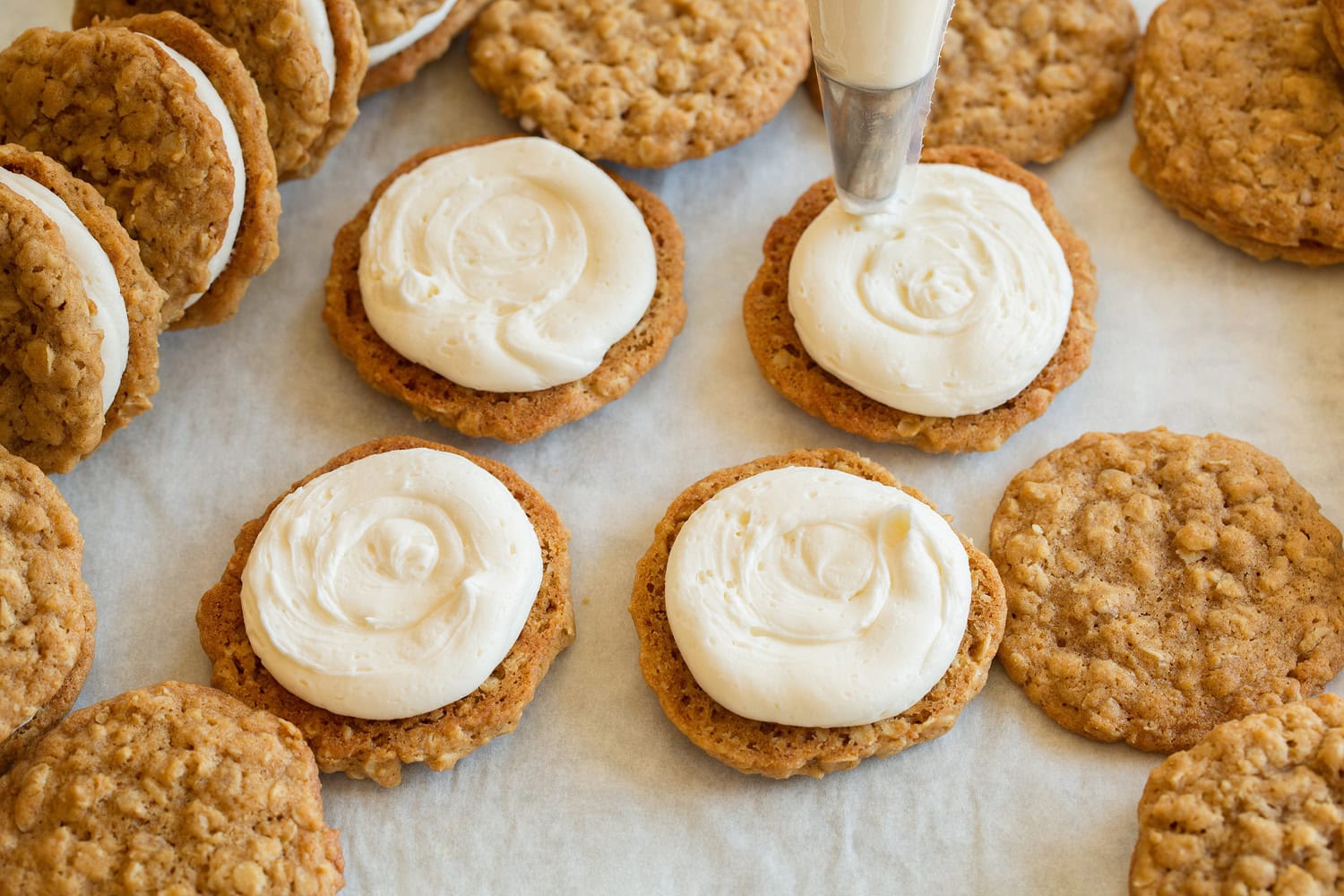 Oatmeal cookies being topped with cream pie frosting filling.