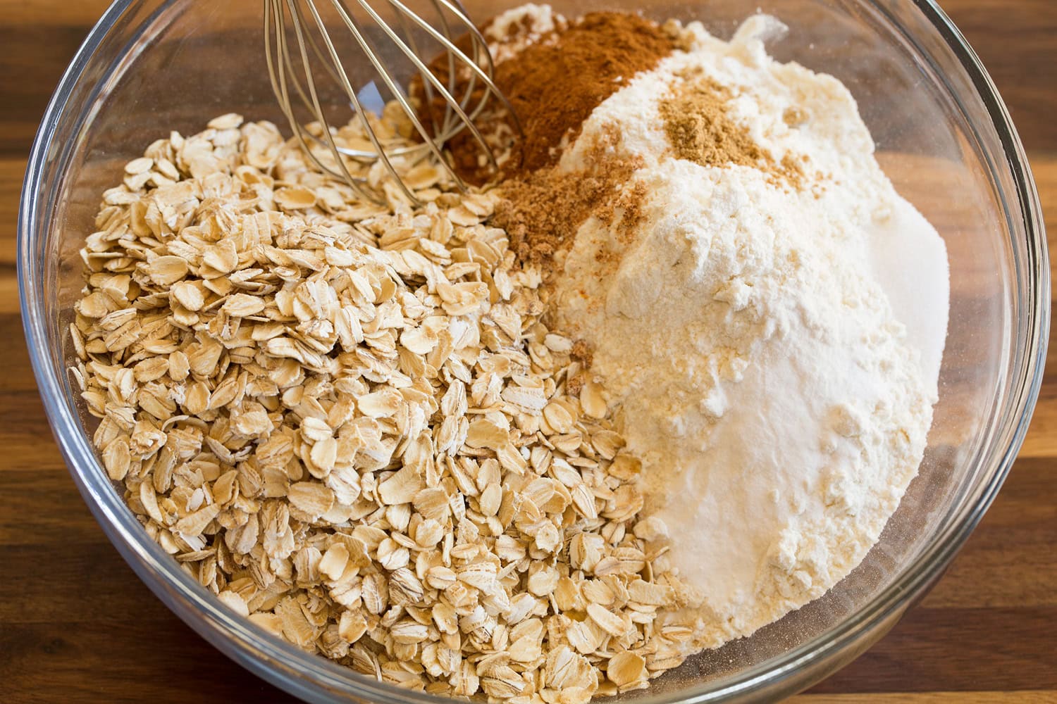 Mixing dry ingredients for oatmeal cookie dough in glass bowl.