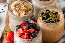 Overnight oats in mason jars, five different ways, on a wooden platter next to a spoon.