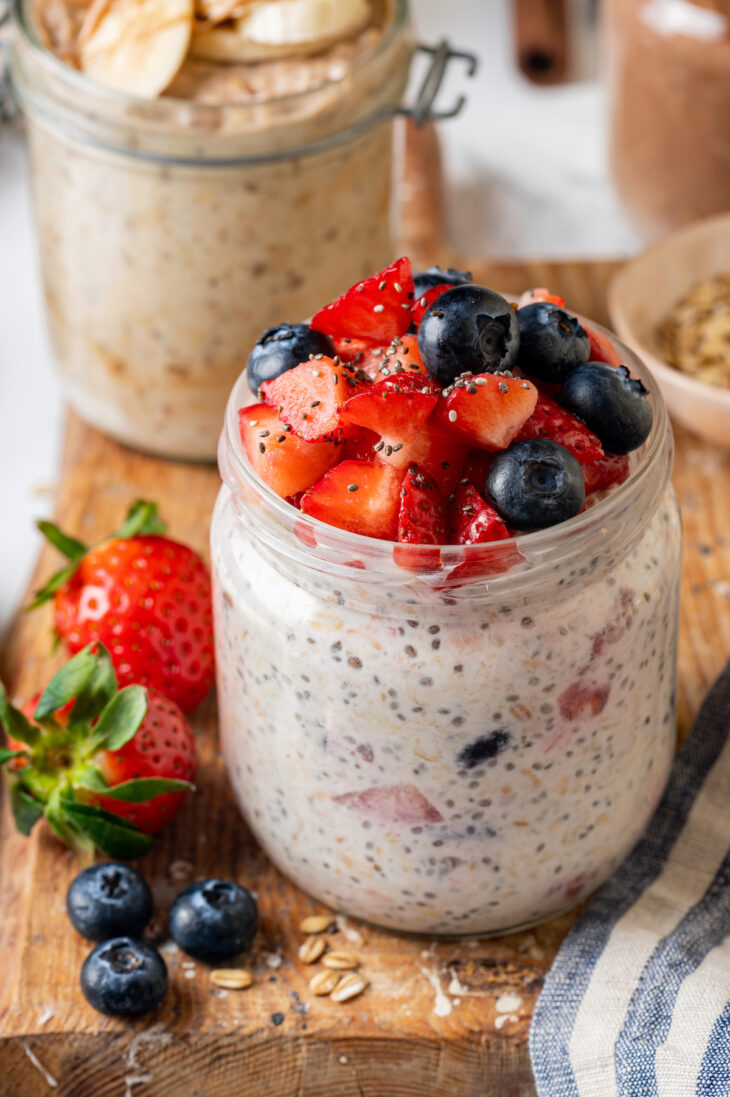 A mason jar of berry chia overnight oats on a wooden platter, with a second jar of overnight oats in the background.