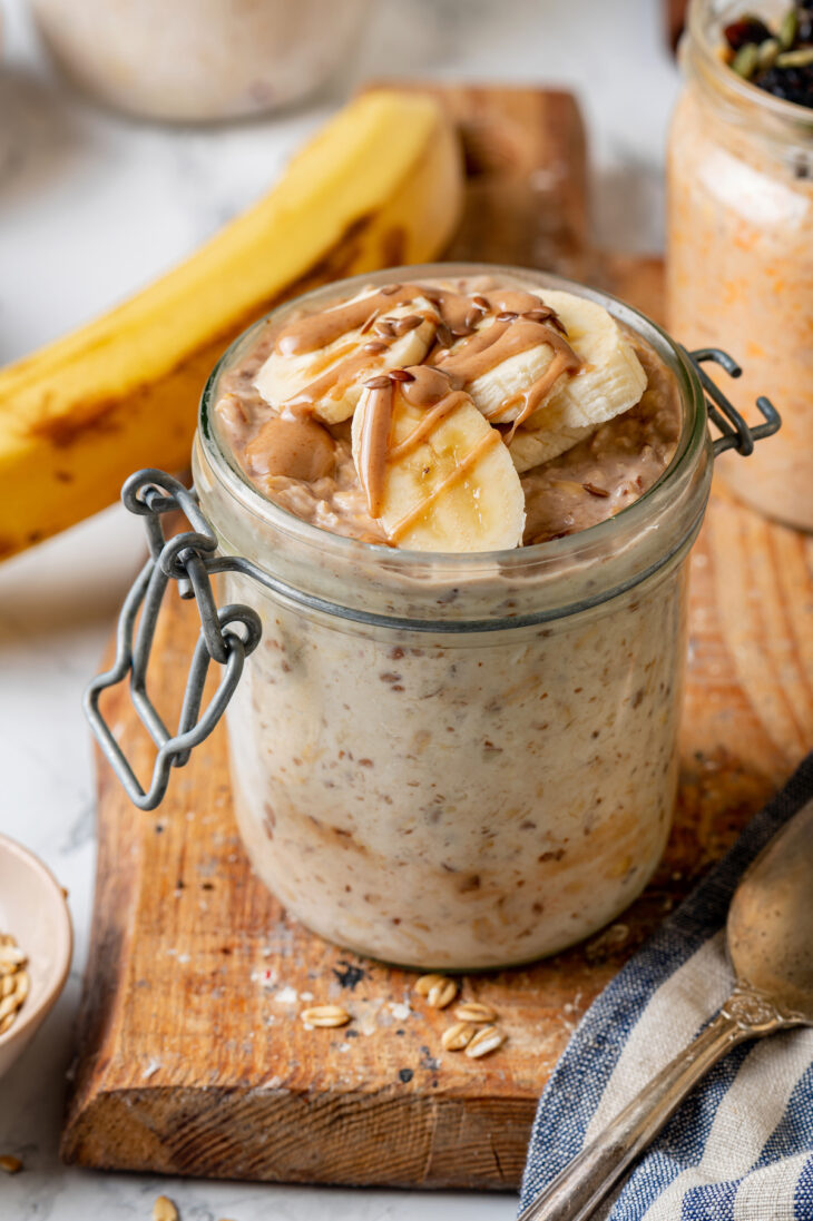 A mason jar of banana flax overnight oats on a wooden platter, with a whole banana in the background.