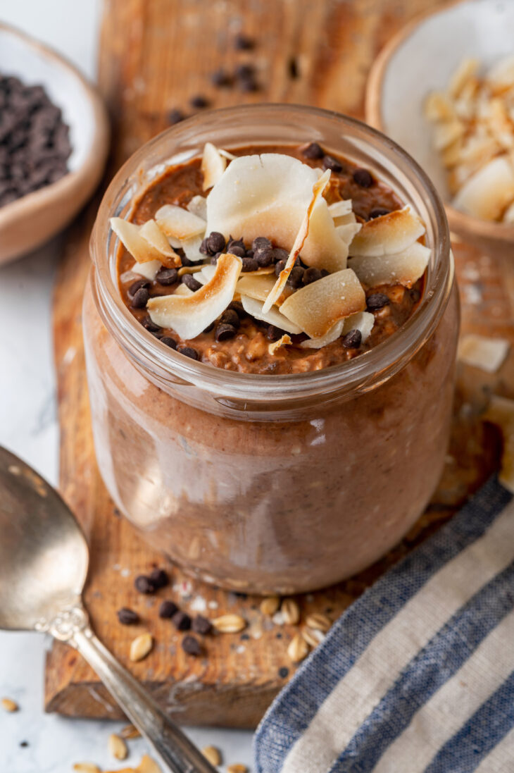 A mason jar of chocolate peanut butter overnight oats on a wooden platter.