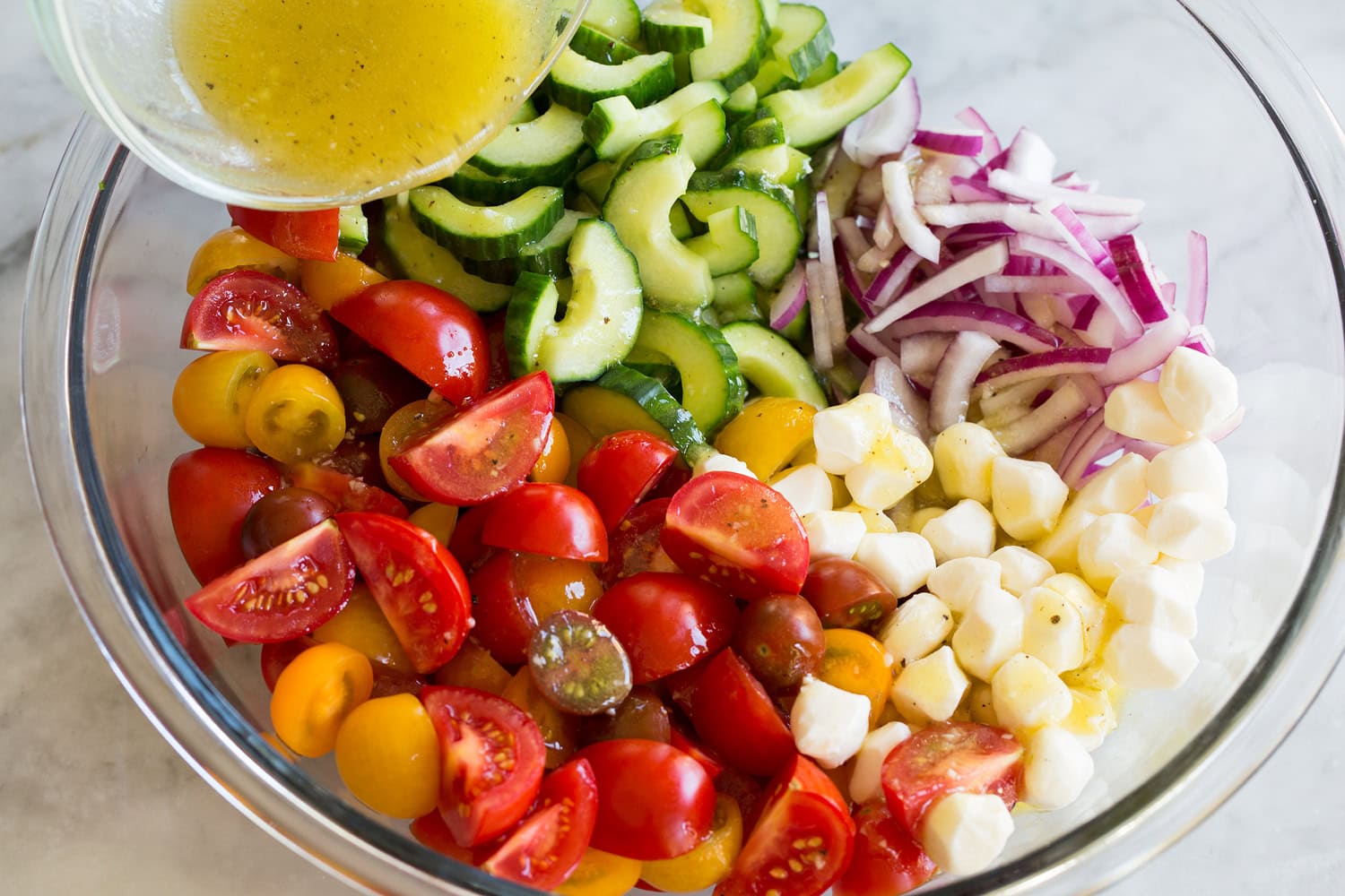 Panzanella salad ingredients in a mixing bowl with dressing being poured over.