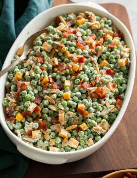 Pea salad with cheddar and bacon shown in an oval serving dish over a wooden board.