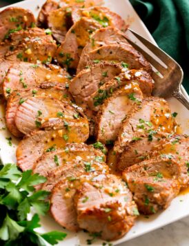 Sliced baked pork tenderloin on a platter with pan sauce.