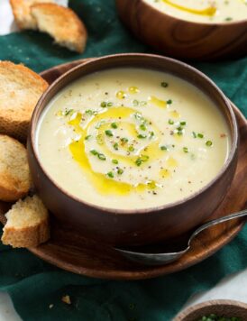 Close up photo of potato leek soup in a wooden bowl garnished with chives and olive oil.