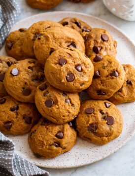 Image of pumpkin chocolate chip cookies stacked on a white serving plate.