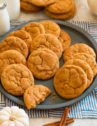 Pumpkin snickerdoodle cookies on a blue plate with white pumpkins and cinnamon sticks around it for decoration.