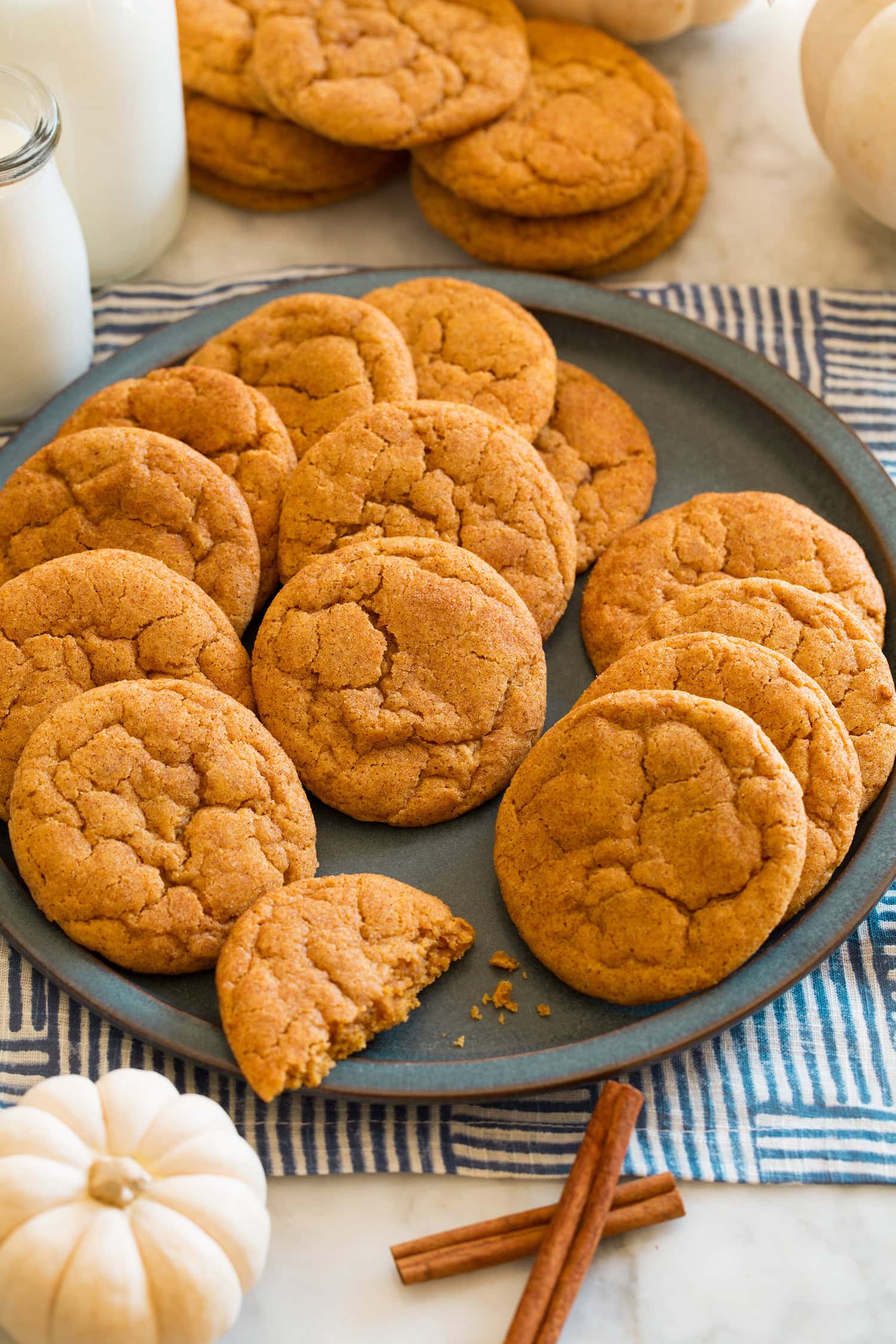 Pumpkin snickerdoodle cookies on a blue plate with white pumpkins and cinnamon sticks around it for decoration.