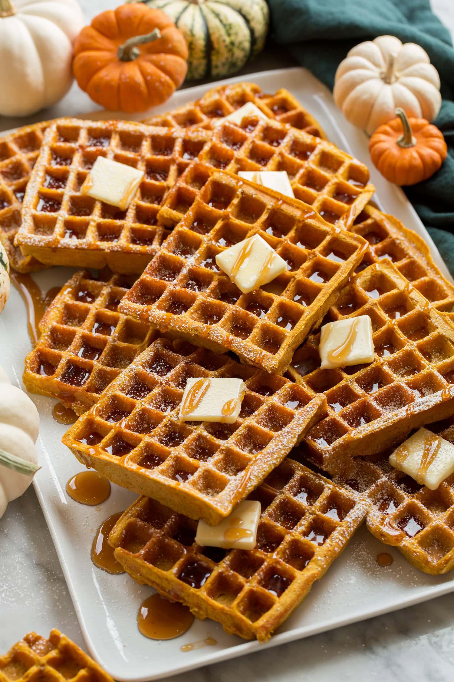 Stacked homemade pumpkin waffles on a platter shown from a the side.