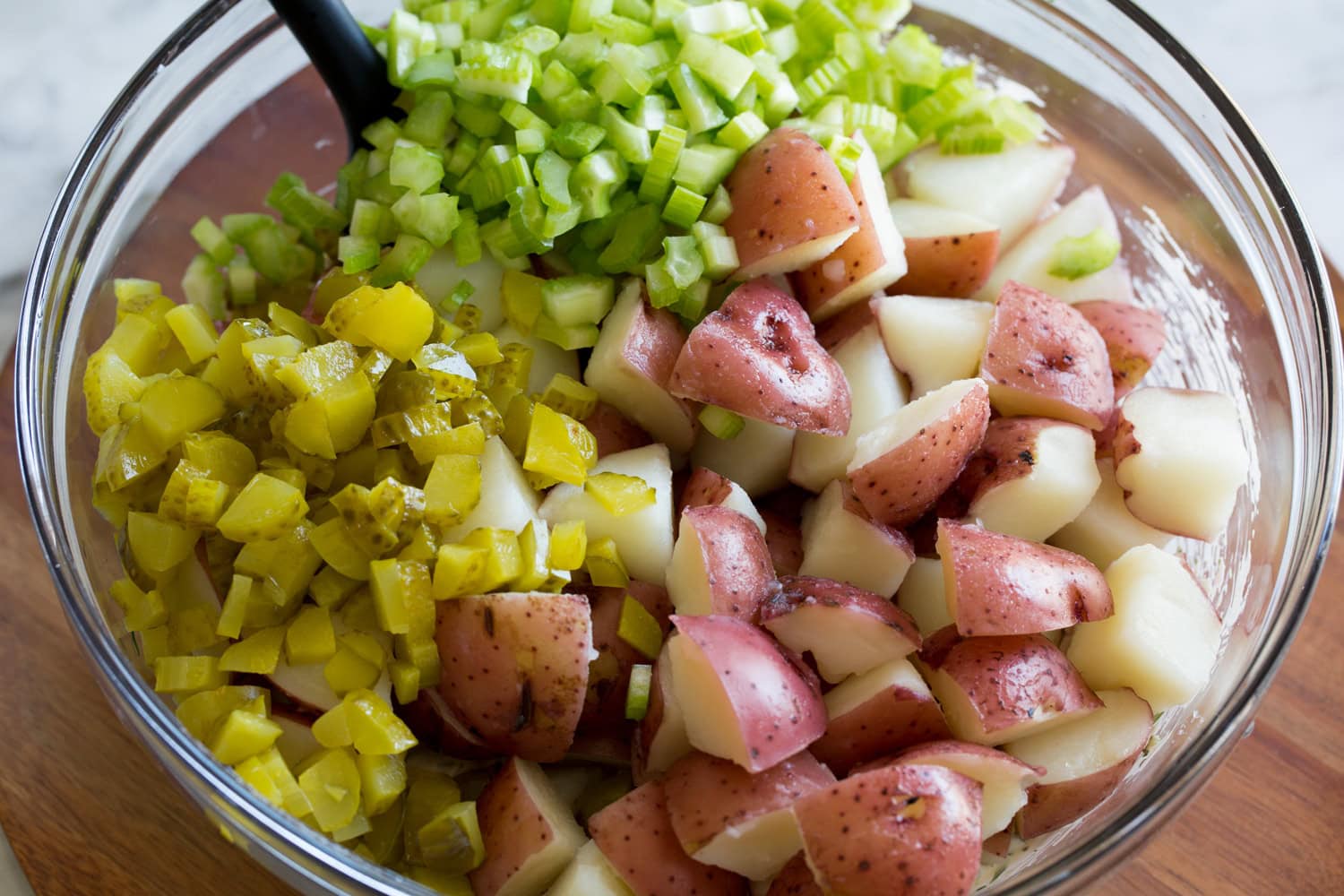 Potatoes, celery and pickles added to mixing bowl with dressing.