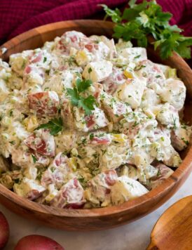 Red Potato Salad in a wooden bowl shown garnished with fresh parsley and dill.